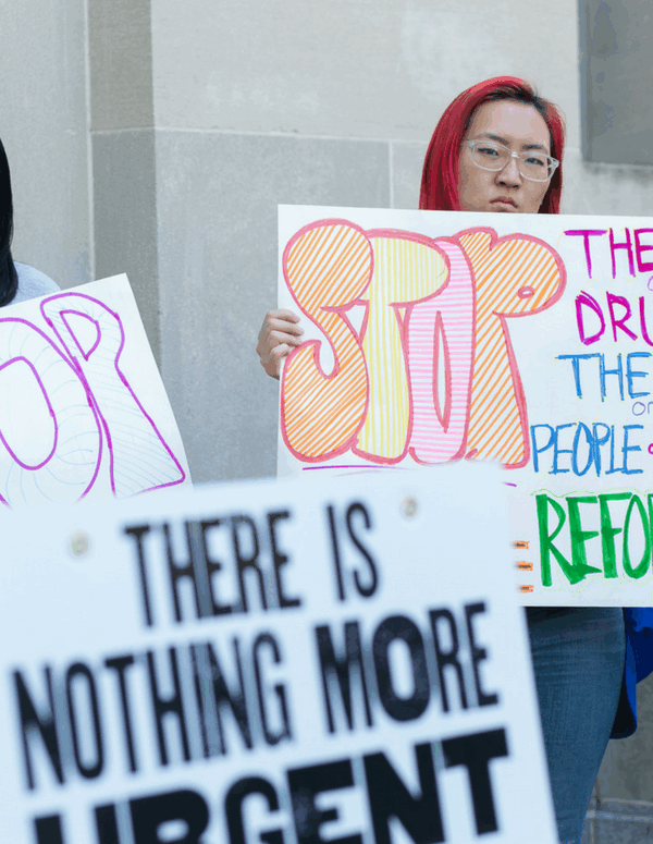 Protesters holding signs that say Stop The War on Drugs, the war on people of color, reform now.