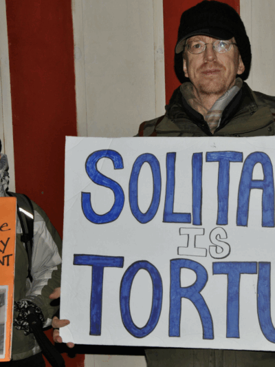 A man holding a sign that says "Solitary Is Torture"