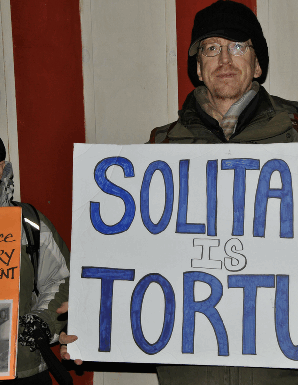 A man holding a sign that says "Solitary Is Torture"
