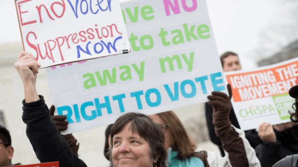 A white woman holding a sign that says "End Voter Suppression Now"