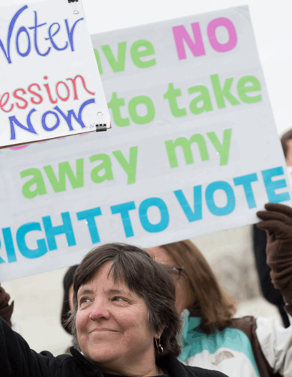 A white woman holding a sign that says "End Voter Suppression Now"