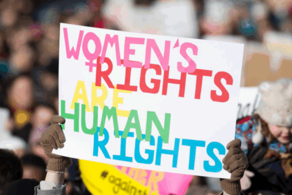 picture from the 2018 Women's March in Richmond, of a dark-skinned woman holding a sign that said "women's rights are human rights" and another white woman holding a sign that said "Power to the Polls"