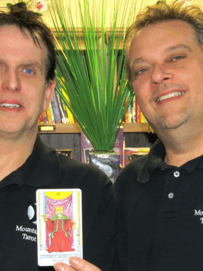 Picture of our client Mark Mullins and his husband, Jerome, holding a Tarot card that says "Justice"