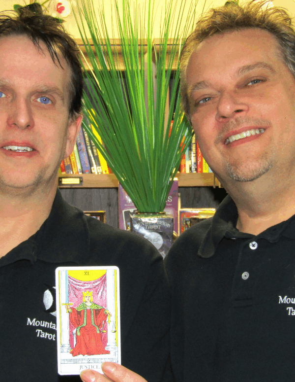 Picture of our client Mark Mullins and his husband, Jerome, holding a Tarot card that says "Justice"