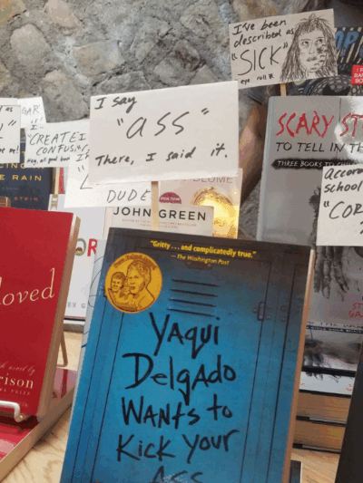 A display of banned books in which the books look like they are holding protest signs about the reasons why they were banned or challenged