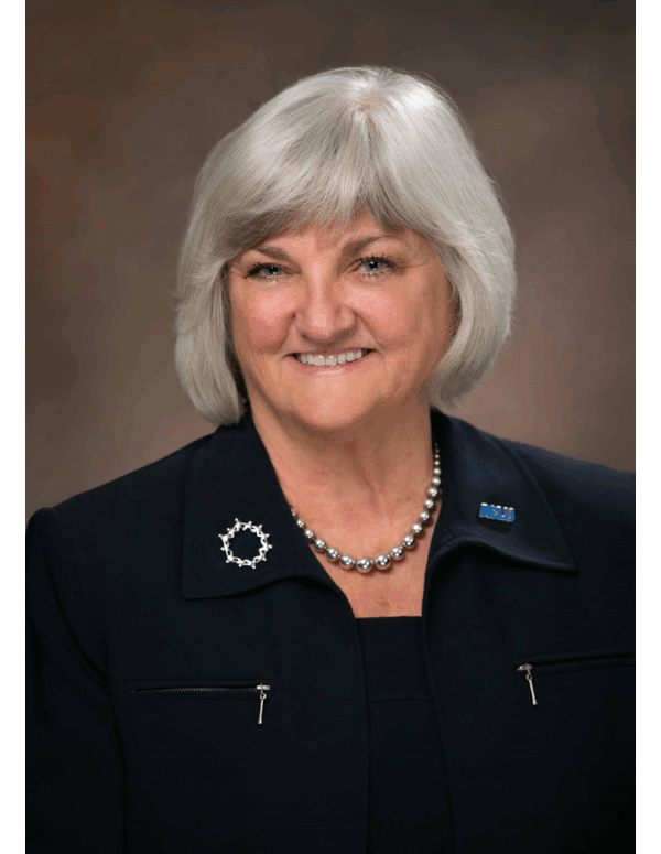 portrait of our executive director Claire Gastanaga, with shoulder length silver hair, round face, blue eyes, and wearing all black.