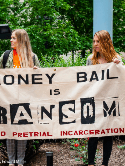 two woman holding a banner that said "money bail is ransom. End pretrial incarceration."