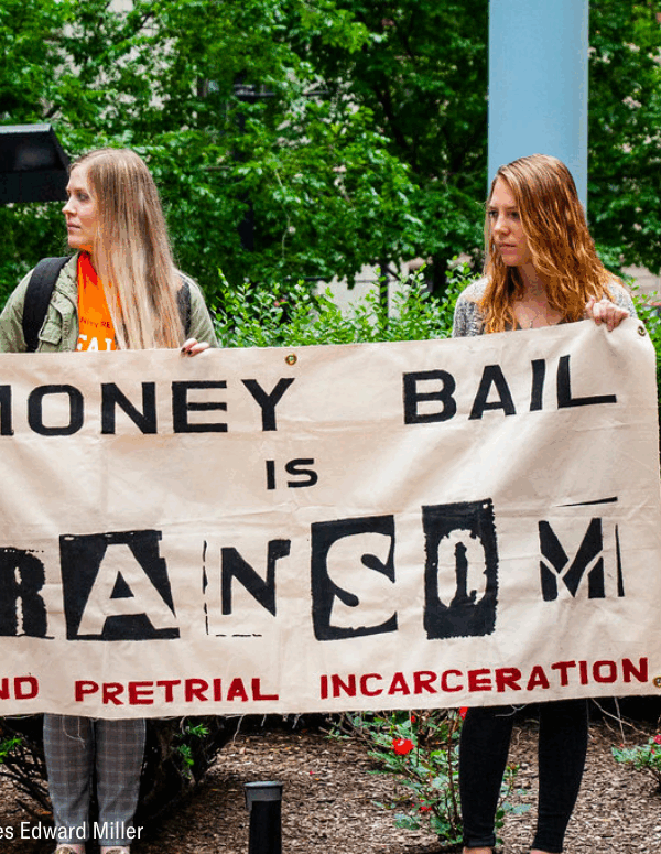 two woman holding a banner that said "money bail is ransom. End pretrial incarceration."