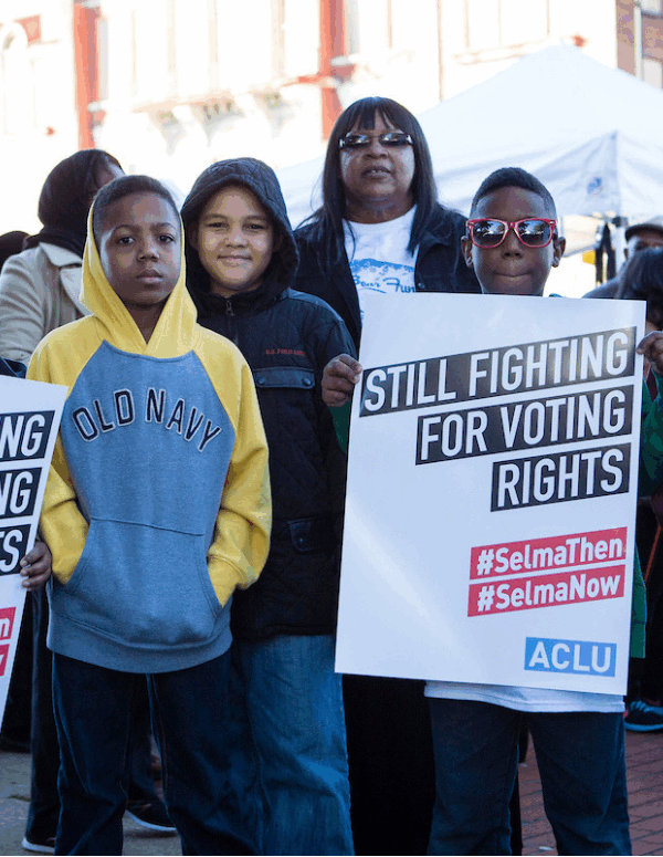 A group of black youths holding signs that say "still fighting for voting rights"