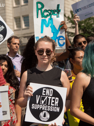 protesters holding signs that say "respect my vote" and "end voter suppression"