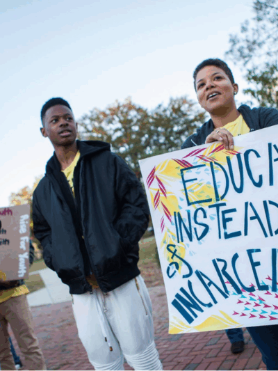 a black woman holding a sign that says "educate instead of incarcerate"