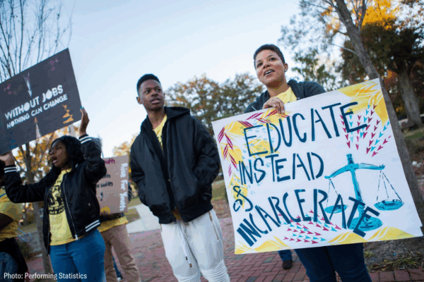 a black woman holding a sign that says "educate instead of incarcerate"