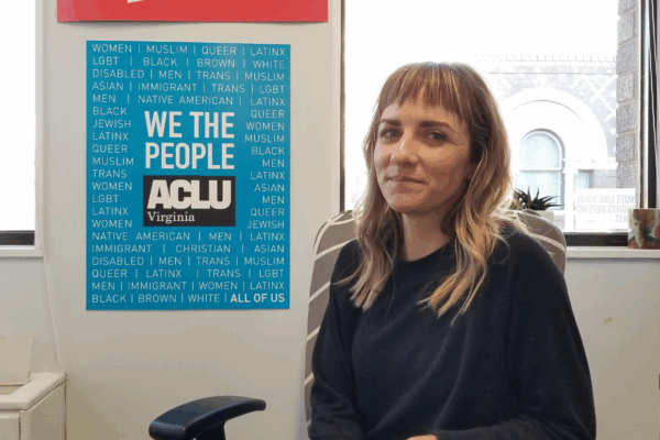 portrait of our client Katie Carline, a petite blonde woman with blue eyes wearing a navy blue sweater, next to an ACLU-VA poster