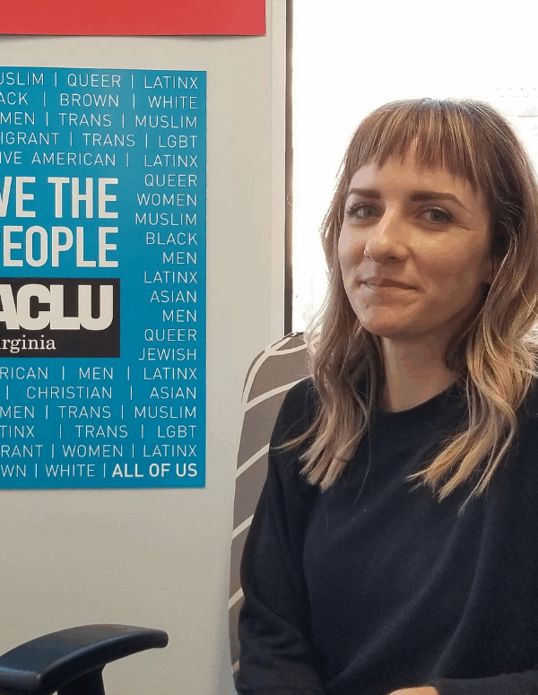 portrait of our client Katie Carline, a petite blonde woman with blue eyes wearing a navy blue sweater, next to an ACLU-VA poster