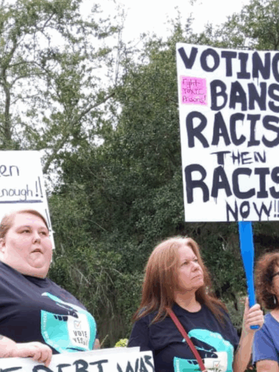 protesters holding a sign that says "voting bans: racist then, racist now"