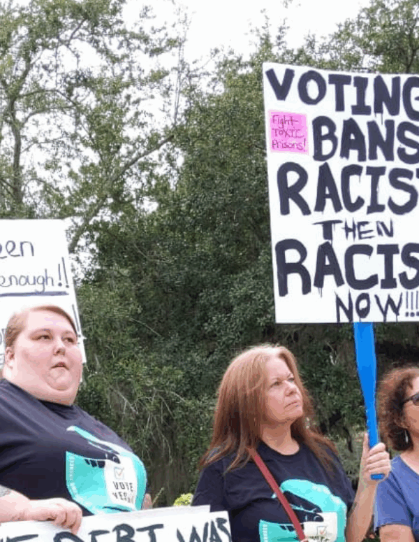 protesters holding a sign that says "voting bans: racist then, racist now"