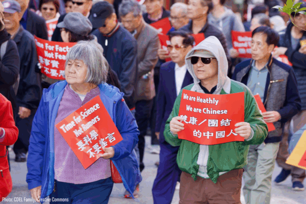 two Asian Americans holding protest signs that say "time for science, not rumors" and "we are chinese, we're healthy"