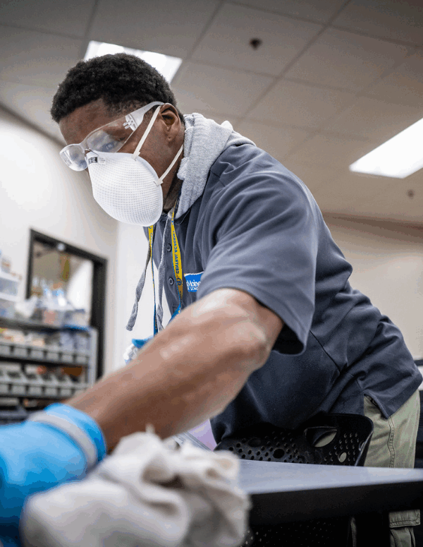 a Black man wearing a mask and cleaning a table during the COVID-19 pandemic