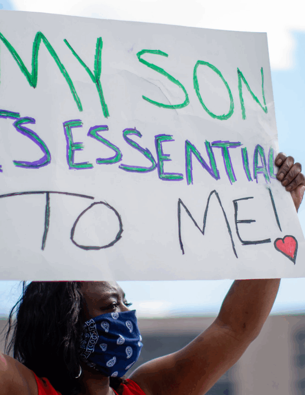 a black woman wearing mask and holding a sign that says "my son is essential to me"