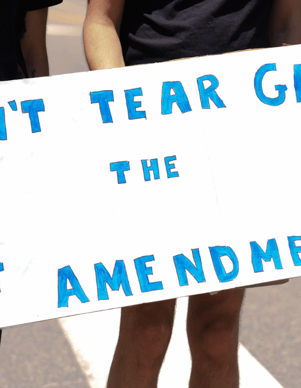 a white sign with blue text that says "don't tear gas the first amendment"