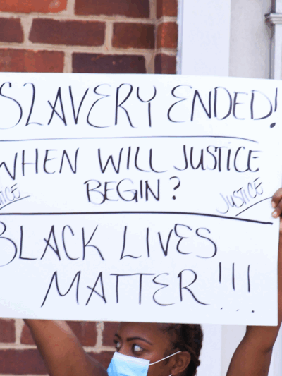 Black woman holding a protest sign that says "slavery ended, when will justice begin? Black lives matter!!!{"