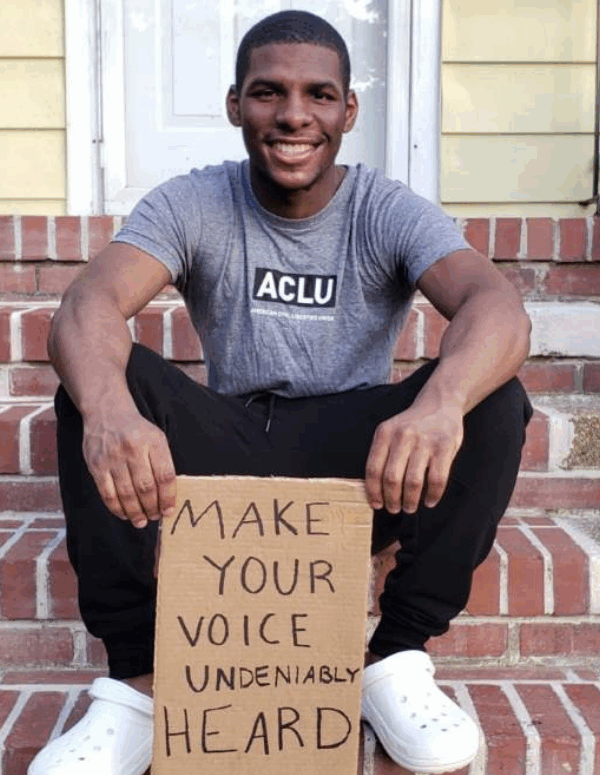 a photo of our intern Alton Coston sitting on the steps in front of his house, holding a cardboard sign that says "make your voice undeniably heard"