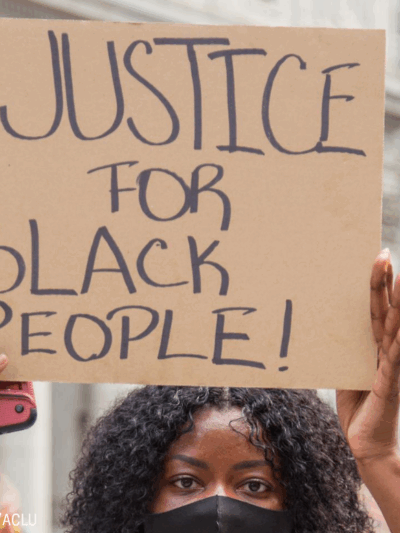 a black woman holding a cardboard sign that says "justice for black people!"