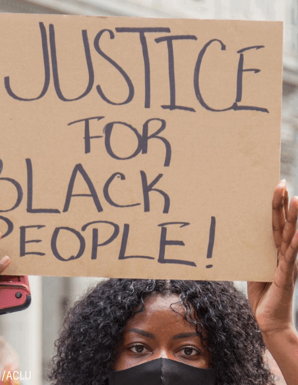 a black woman holding a cardboard sign that says "justice for black people!"