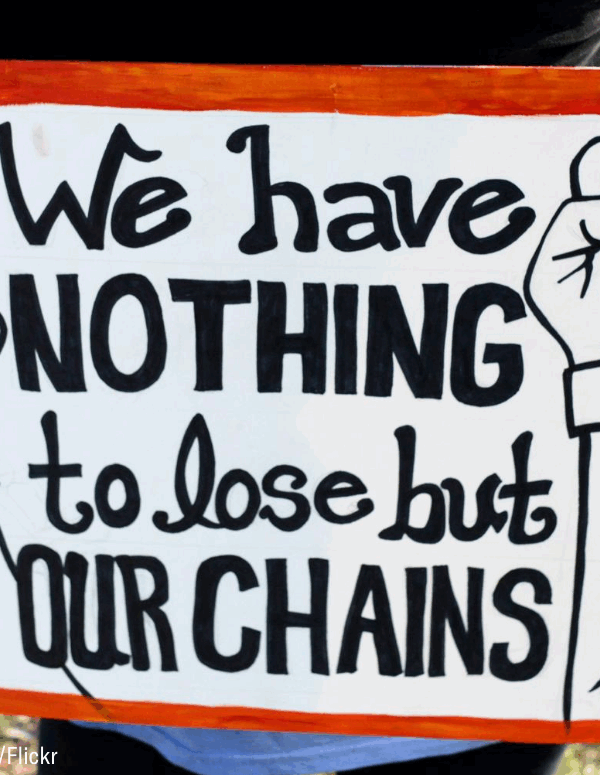 a white sign with red frame with two arms breaking away from a chain, text reads "we have nothing to lose but our chains"
