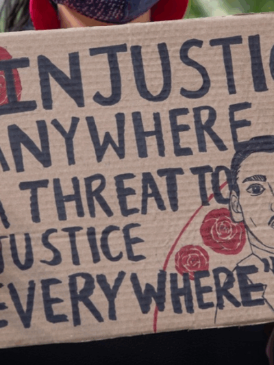 a protester holding a sign that says "injustice anywhere is a threat to justice every where."
