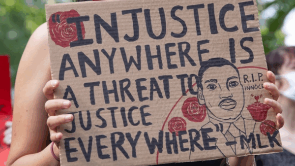 a protester holding a sign that says "injustice anywhere is a threat to justice every where."