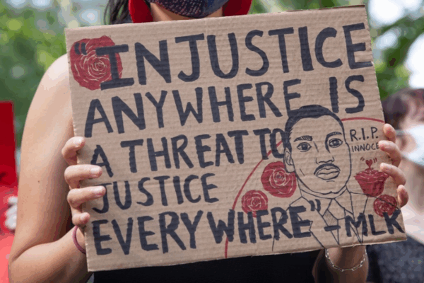 a protester holding a sign that says "injustice anywhere is a threat to justice every where."