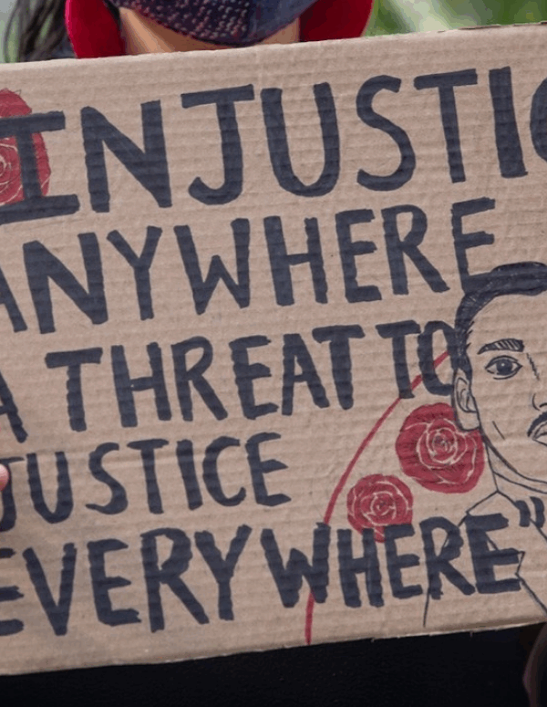a protester holding a sign that says "injustice anywhere is a threat to justice every where."