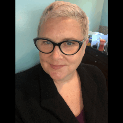 A photo of Mary, a white woman with pixie short blonde hair, wearing a pair of cat eye glasses.
