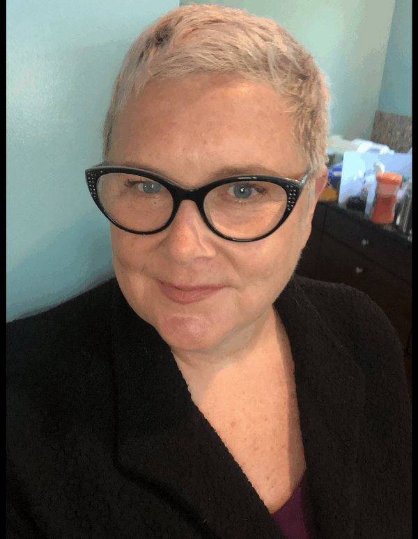 A photo of Mary, a white woman with pixie short blonde hair, wearing a pair of cat eye glasses.