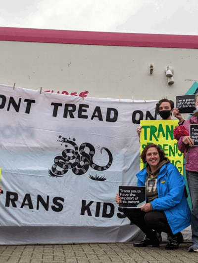 a group of parents and community advocates standing in front of Studio Two Three truck with a banner in the center that reads "Don't Tread on Trans Kids". Community members held pro-trans rights signs like "Let students thrive" and "Trans kids are our kid