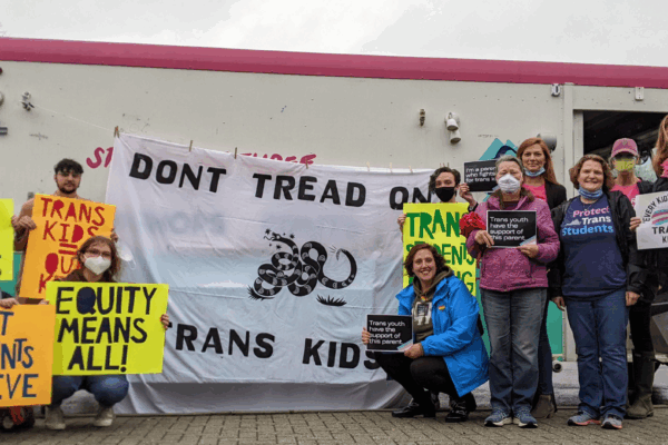 a group of parents and community advocates standing in front of Studio Two Three truck with a banner in the center that reads "Don't Tread on Trans Kids". Community members held pro-trans rights signs like "Let students thrive" and "Trans kids are our kid