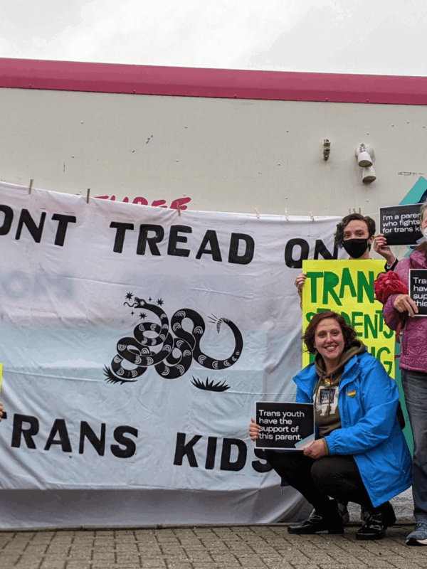 a group of parents and community advocates standing in front of Studio Two Three truck with a banner in the center that reads "Don't Tread on Trans Kids". Community members held pro-trans rights signs like "Let students thrive" and "Trans kids are our kid