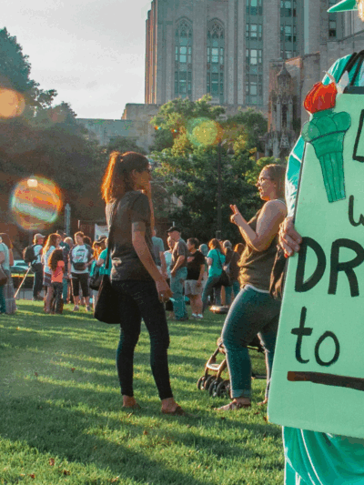 a protester dressed as Lady Liberty held a protest sign that says "Lady Liberty Wants Dreamers to Stay."