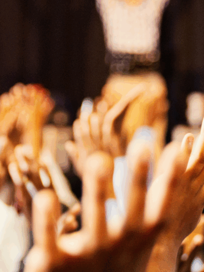 In the foreground a bunch of students' hands are raised, following an instructor in the background