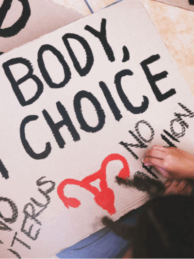 A protester in the process of writing on their sign, which reads "my body, my choice, no uterus, no opinion."