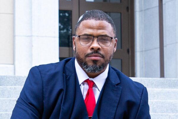 Shawn Barksdale dressed in a navy suit with red tie smiling at the camera