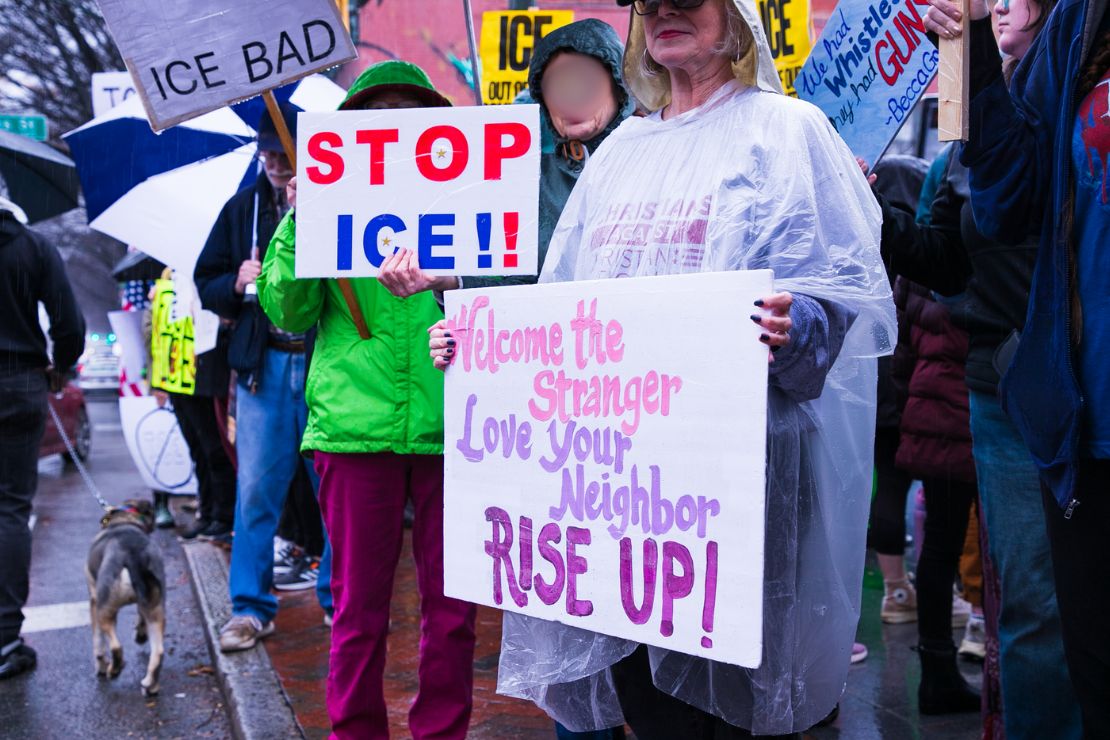 photo of two protesters, one with the sign "Stop ICE" and another with the sign "Welcome the stranger, Love your neighbors, rise up!"