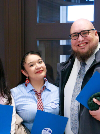 Three people smile towards the camera while holding blue folders.