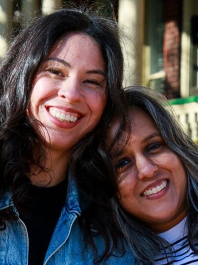 Two women smile towards a camera.
