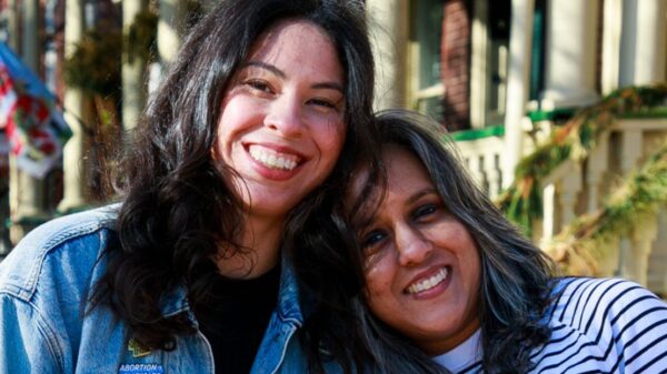 Two women smile towards a camera.