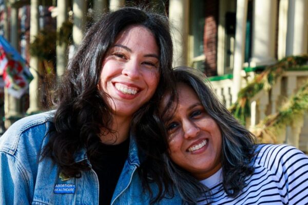 Two women smile towards a camera.