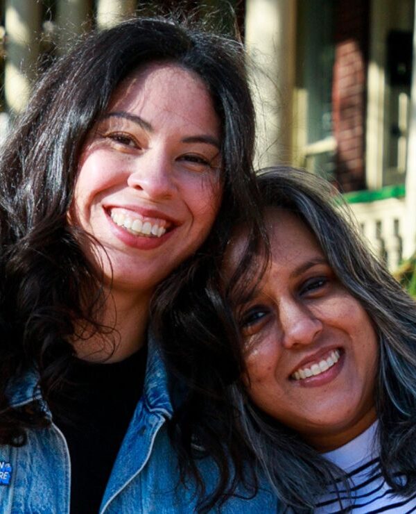 Two women smile towards a camera.