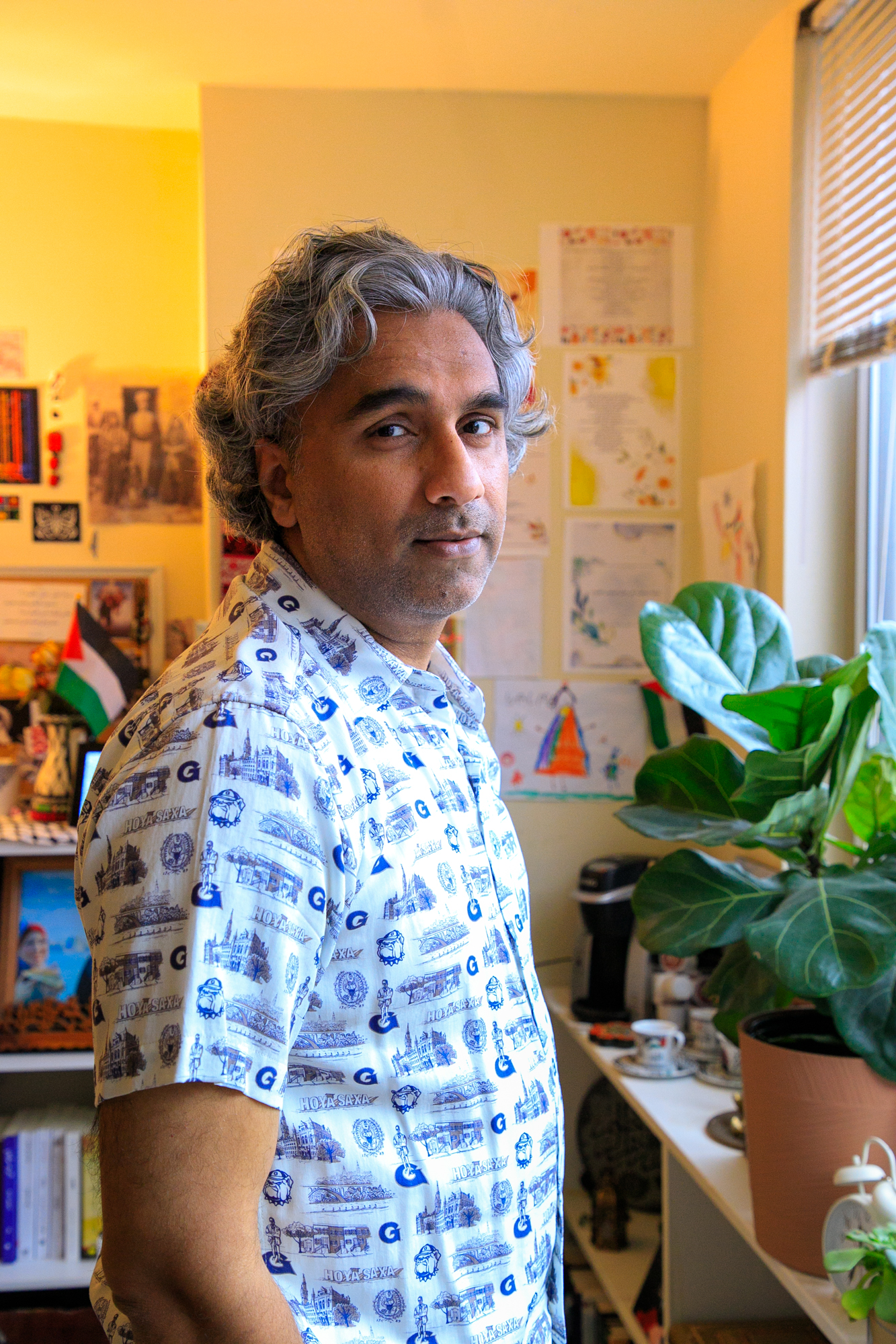 Badar looks at the camera as he stands by the window with the light filling into the room