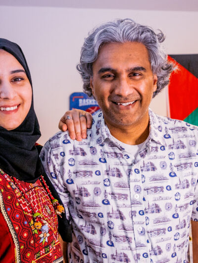 Badar stands next to his wife and smiles with the Palestinian flag in the background